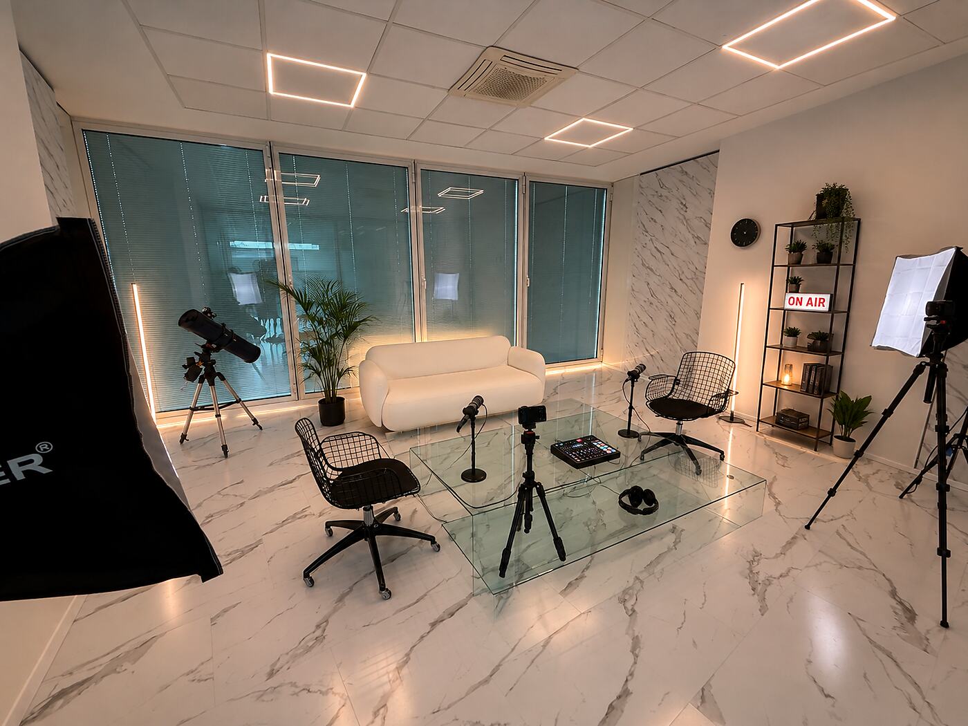 Sala 05 di Narciso Studios, salotto podcast con divano e poltrone attorno a un tavolino in vetro, doppio microfono, mixer e cuffie pronti, pareti in marmo e vetrate a tutta altezza